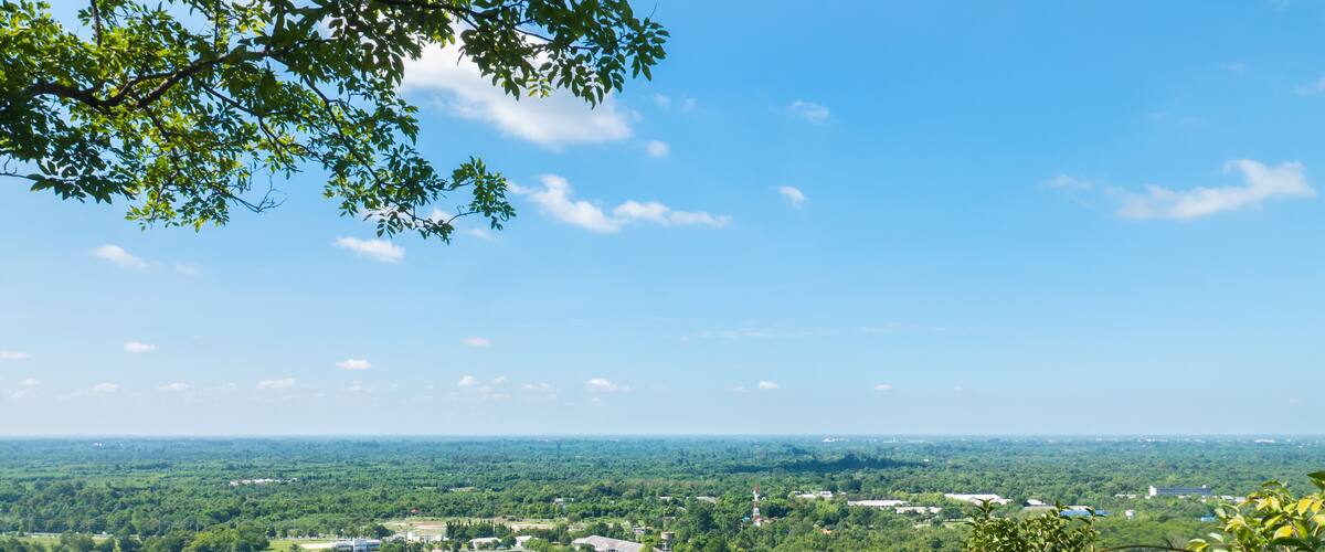 A panoramic view of a lush green landscape with a mix of natural and developed areas, including a large open field and several buildings.