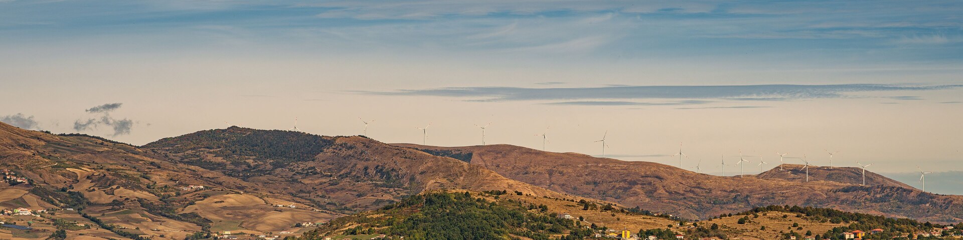 Un pueblo situado en un valle, con aerogeneradores al fondo.