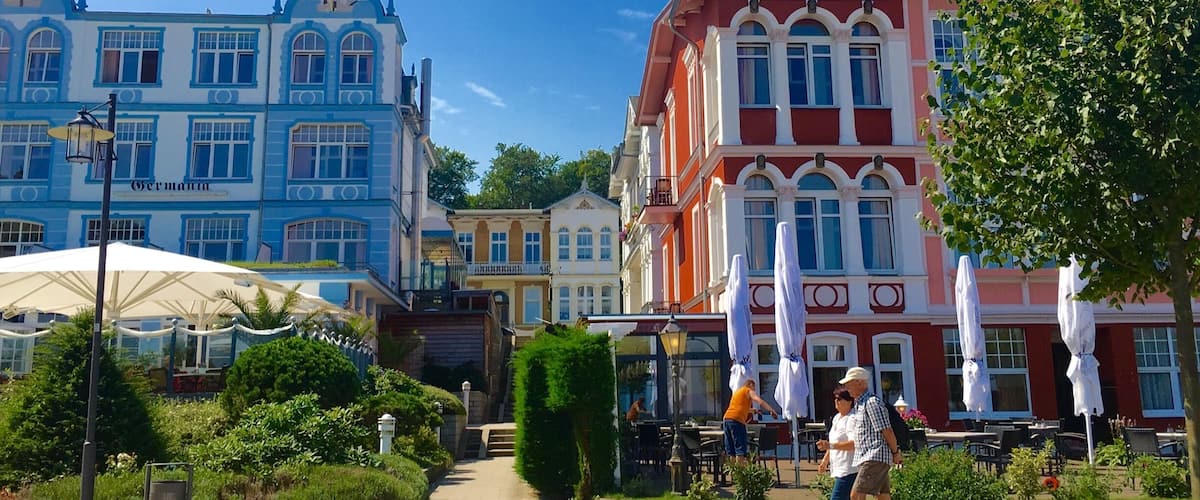 Calle con edificios coloridos, mesas al aire libre y un cielo azul despejado.