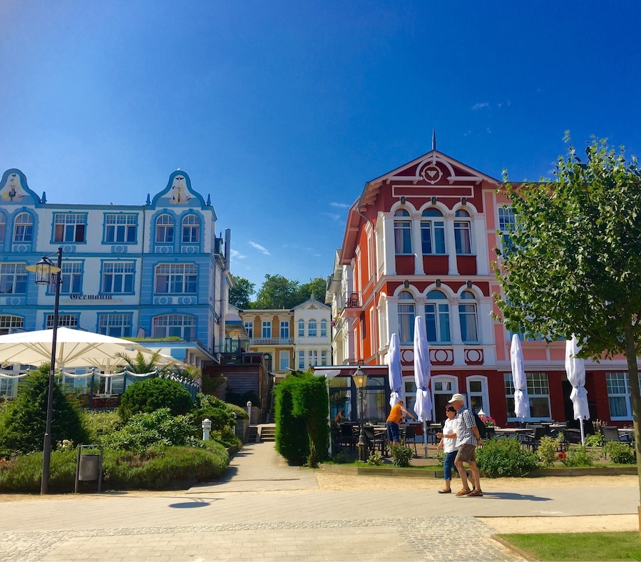 Rua com edifícios coloridos, mesas ao ar livre e um céu azul límpido.
