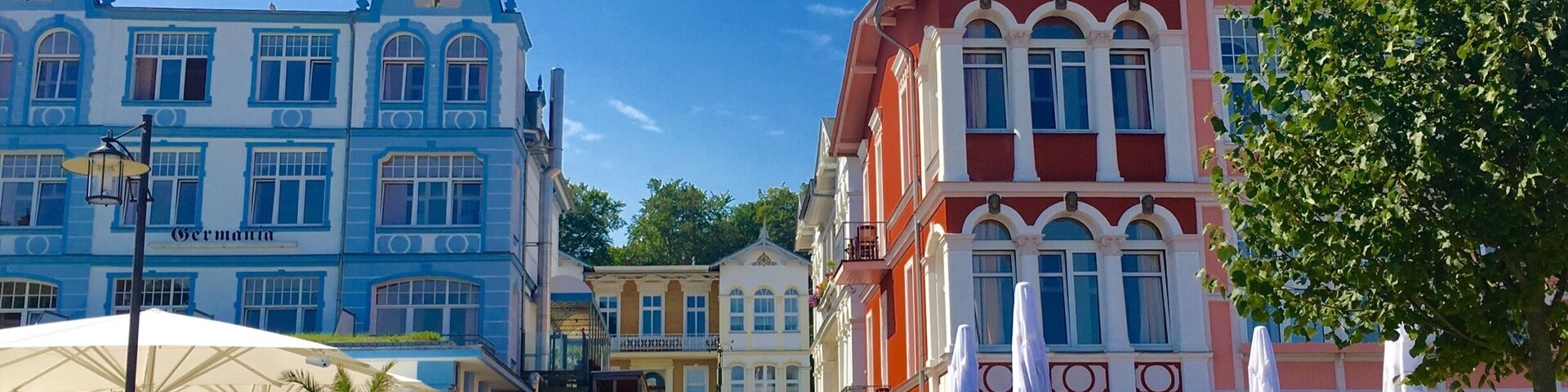Rua com edifícios coloridos, mesas ao ar livre e um céu azul límpido.