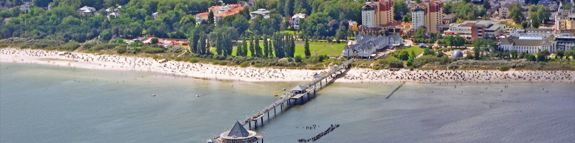 A coastal city with a pier extending into the water, surrounded by buildings and greenery.
