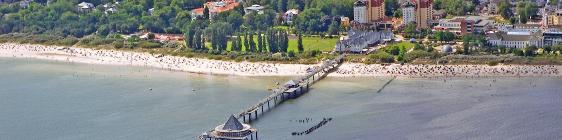 Una ciudad costera con un muelle que se adentra en el agua, rodeada de edificios y vegetación.