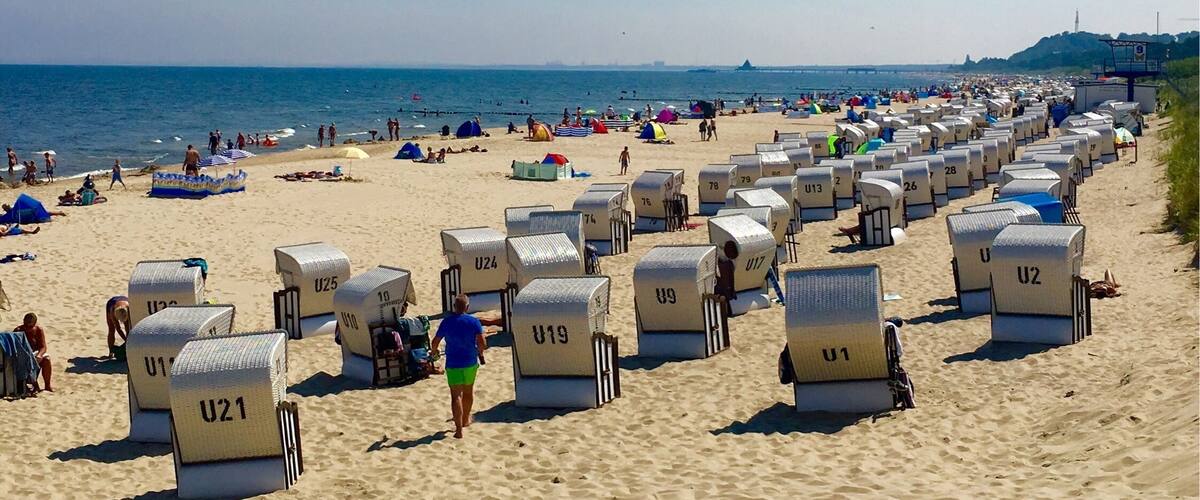 A beach with rows of numbered beach huts and people enjoying the sand and sea.