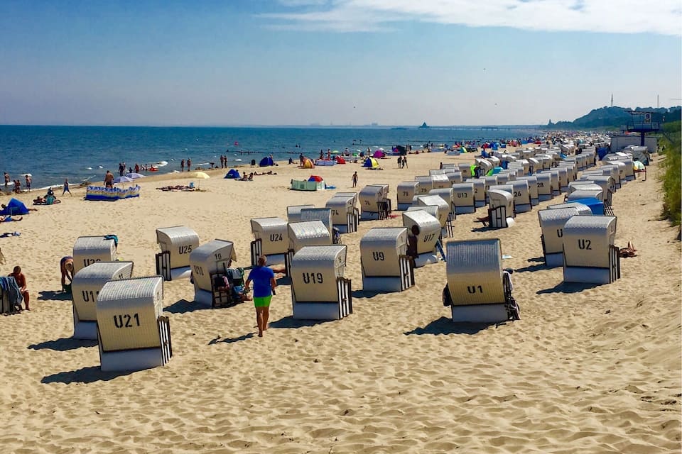 A beach with rows of numbered beach huts and people enjoying the sand and sea.