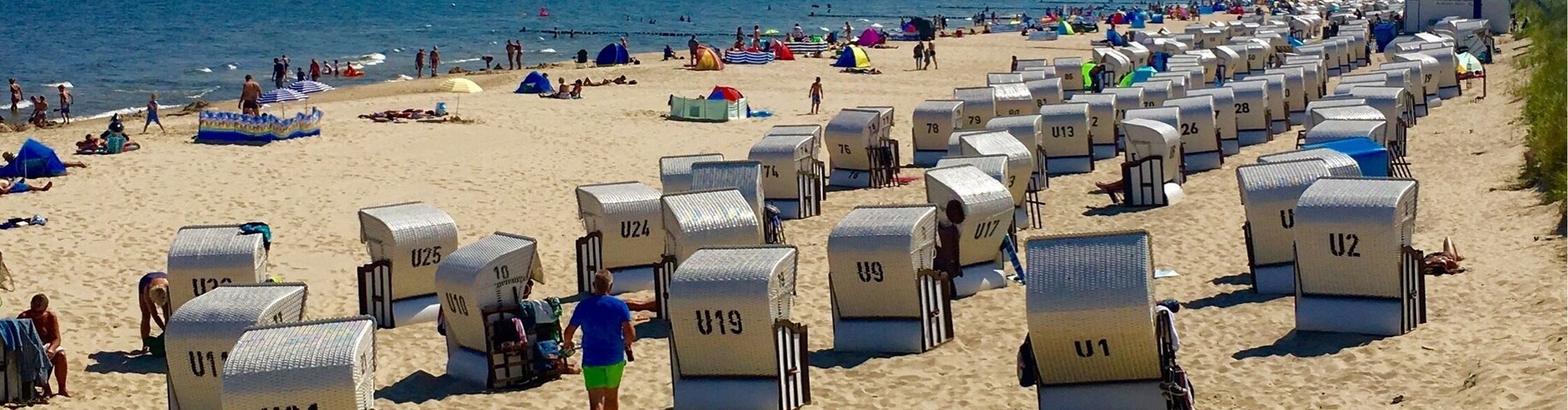 Una playa con filas de cabañas de playa numeradas y gente disfrutando de la arena y el mar.