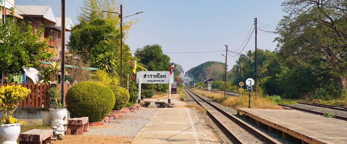 A railway platform with a sign in a foreign language, tracks, and surrounding greenery.