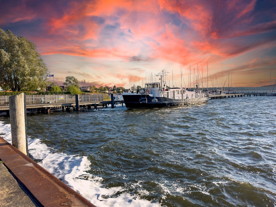 Un port avec un bateau amarré, une jetée s’avançant dans l’eau et un ciel au coucher du soleil.