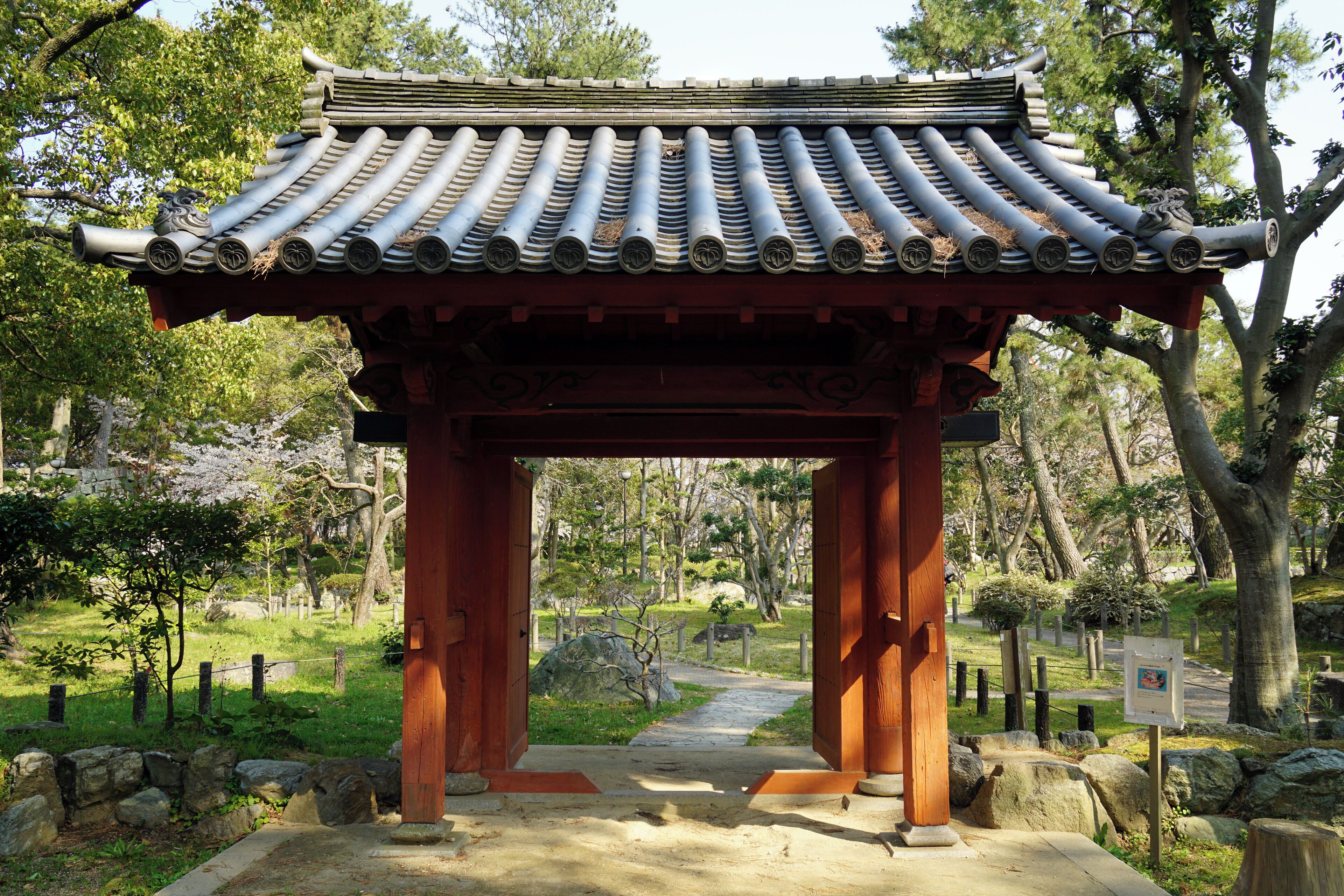A traditional Japanese torii gate with a tiled roof, surrounded by a stone pathway and lush greenery.