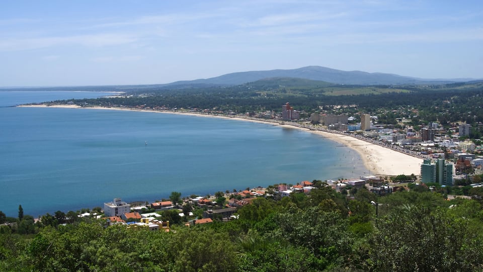 A coastal city with a long sandy beach, dense residential area, and mountains in the background.