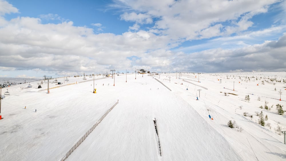 Ein verschneiter Ski-Hang mit Skiliften, Bäumen und blauem Himmel.