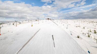 Una pista de esquí nevada con remontes, árboles y un cielo despejado.