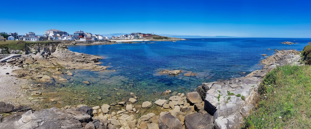 A coastal town with clear blue waters, rocky shores, and buildings along the coastline.