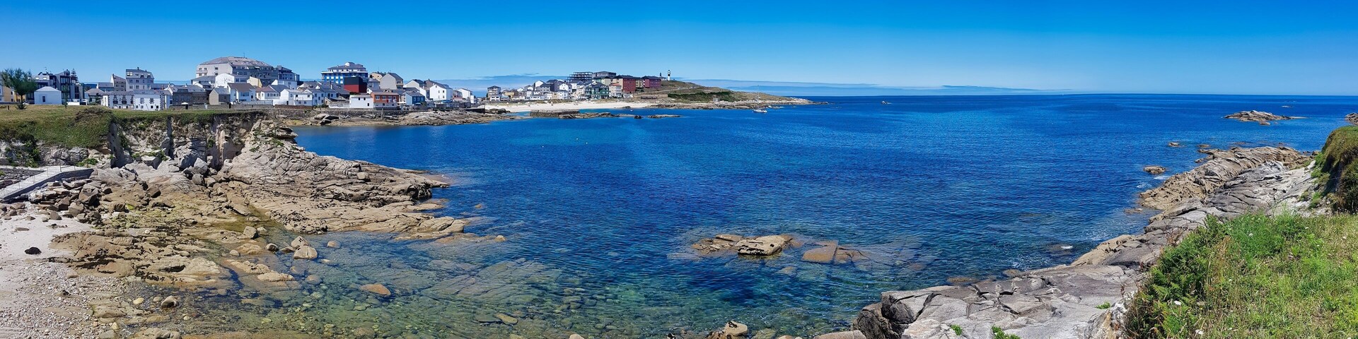 A coastal town with clear blue waters, rocky shores, and buildings along the coastline.