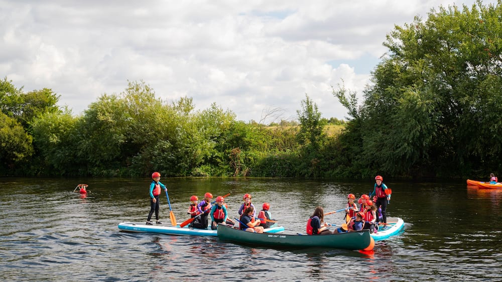 A group of people in canoes on a calm river surrounded by lush greenery.