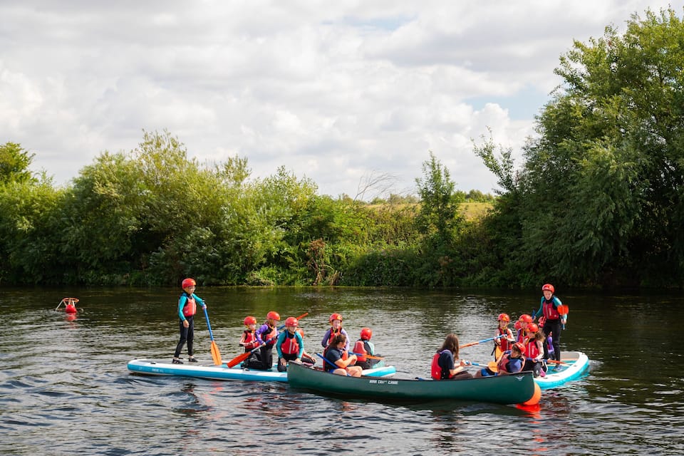A group of people in canoes on a calm river surrounded by lush greenery.