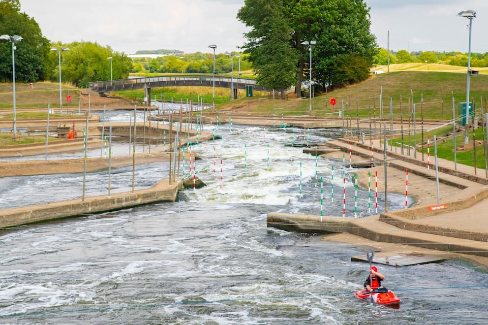 Un riu amb un pont, kayaks i un camp verd.