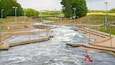A river with a bridge, kayaks, and a green field.