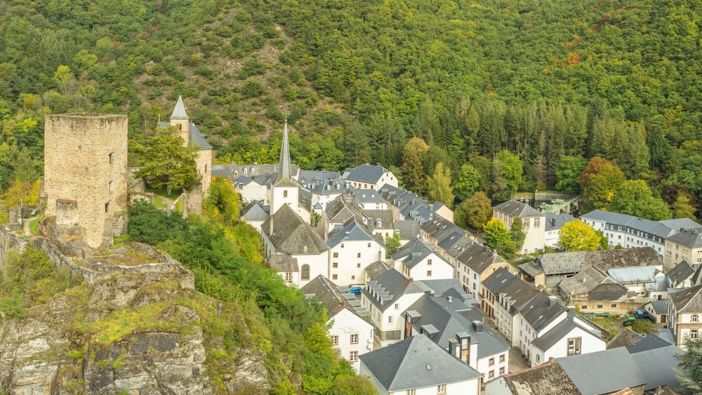 A historic town with a prominent tower, a river, and lush green hills.