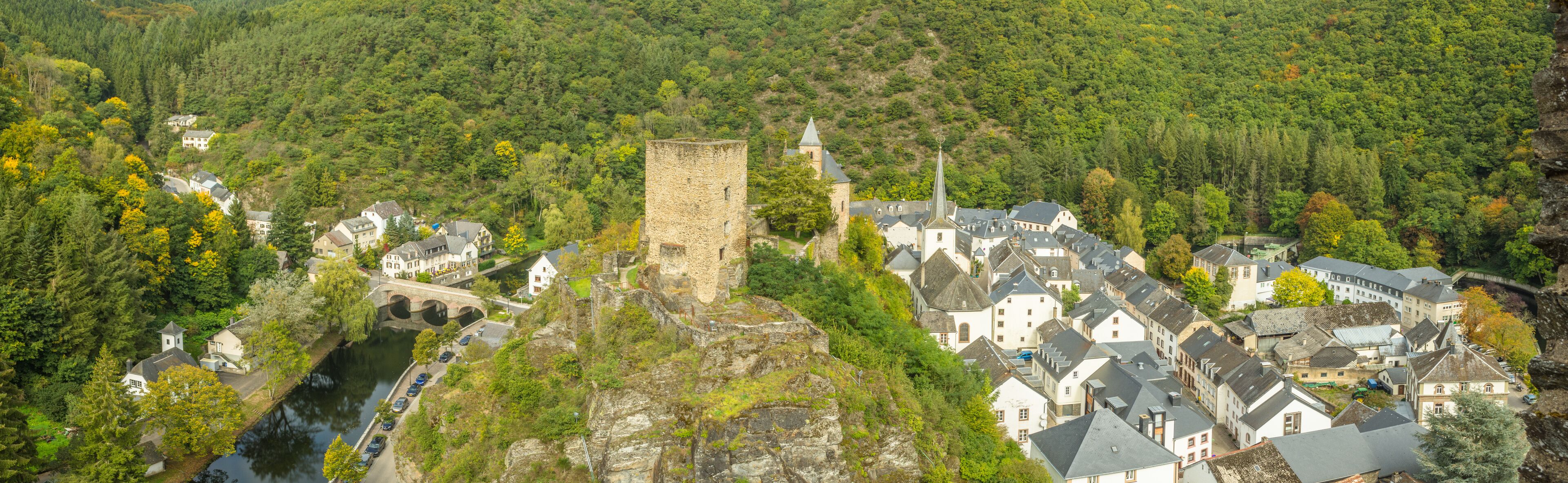 A historic town with a prominent tower, a river, and lush green hills.