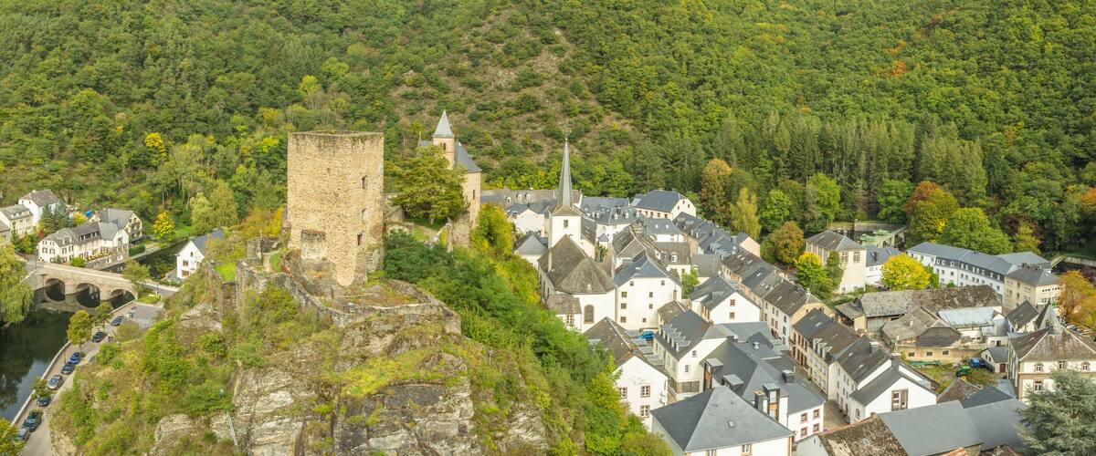 A historic town with a prominent tower, a river, and lush green hills.