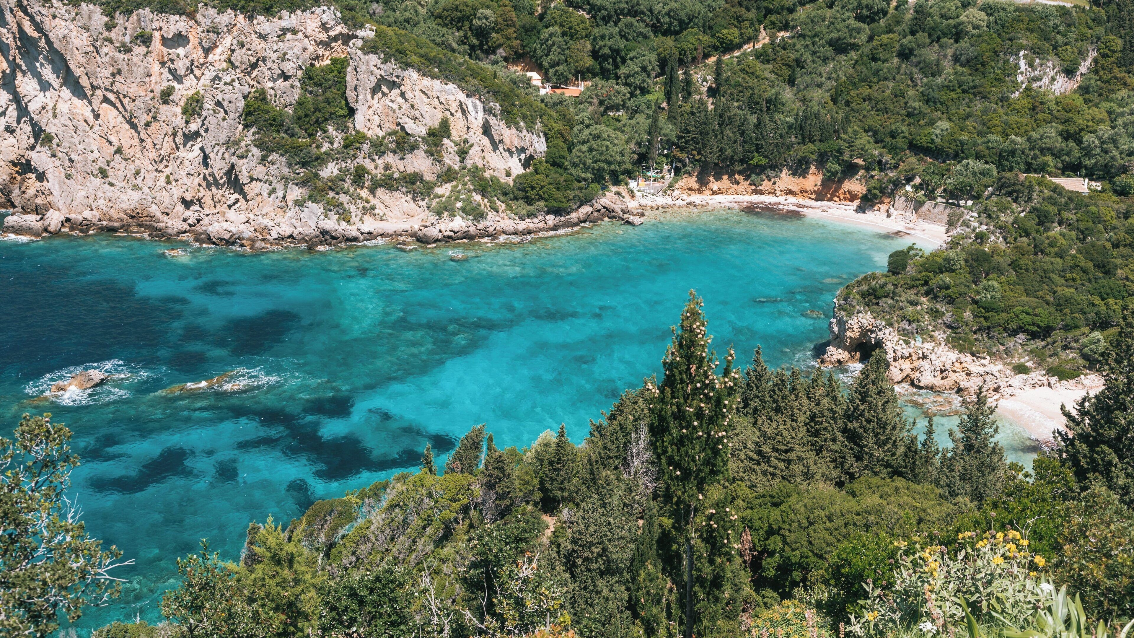 Paisagem costeira com águas turquesa cristalinas, falésias rochosas e vegetação densa.
