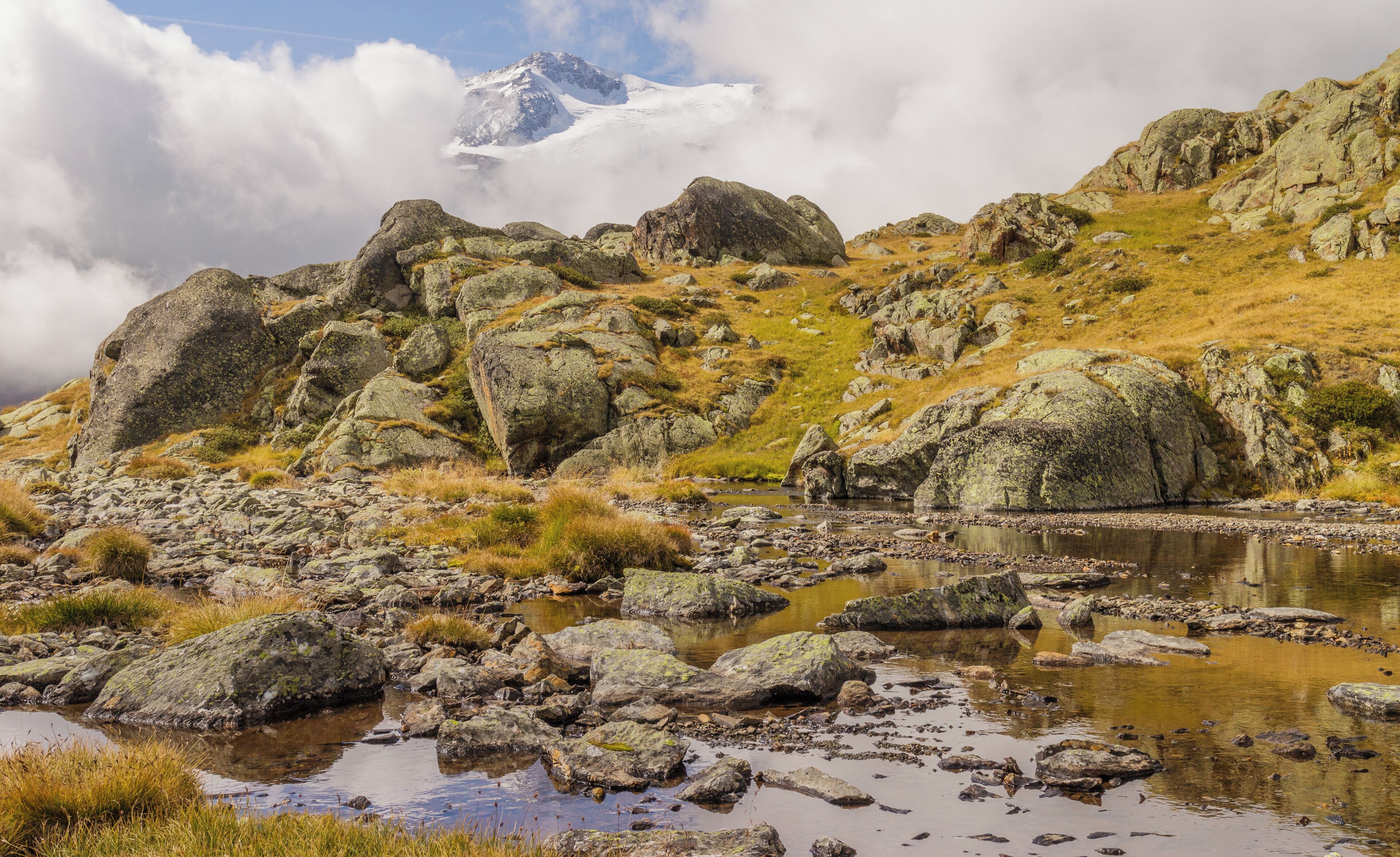 Un paisaje montañoso con terreno rocoso, un pequeño arroyo y un pico nevado a lo lejos.