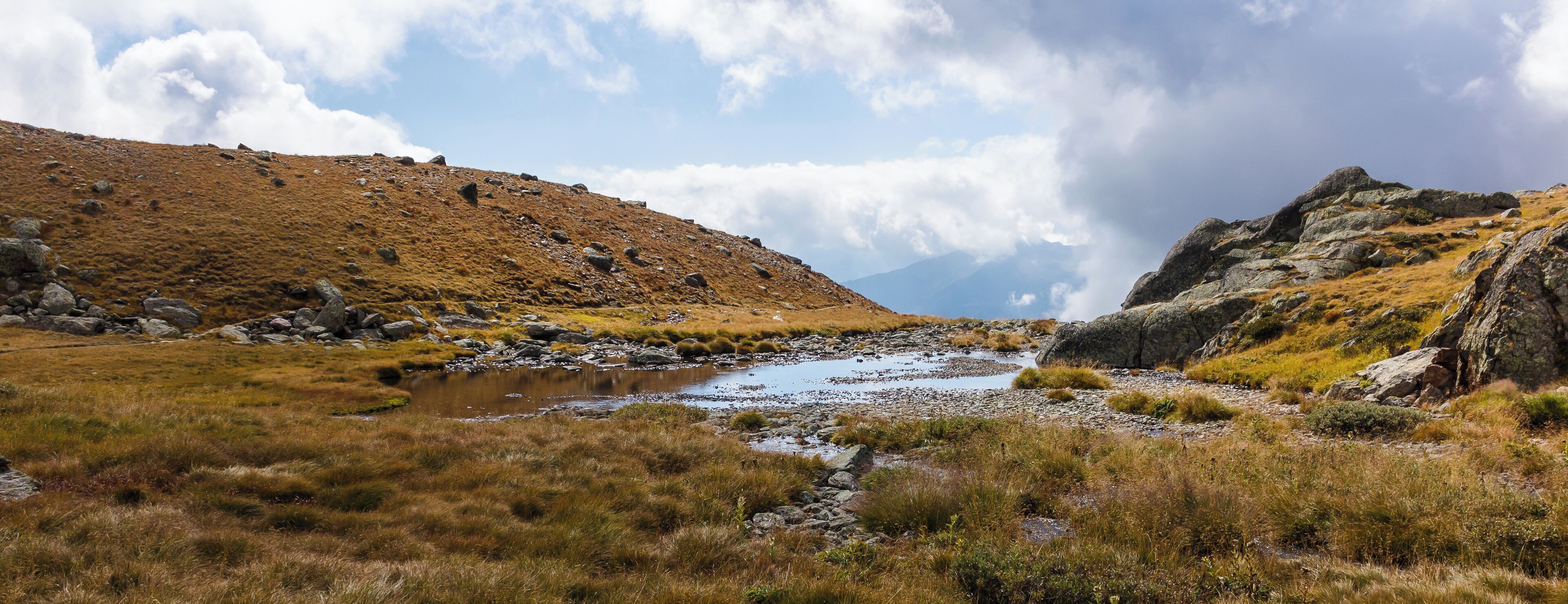 Mountain hiking of parking in power station Malga Mare to Lago Lungo (2553m). Water streams over the mountain plateau.