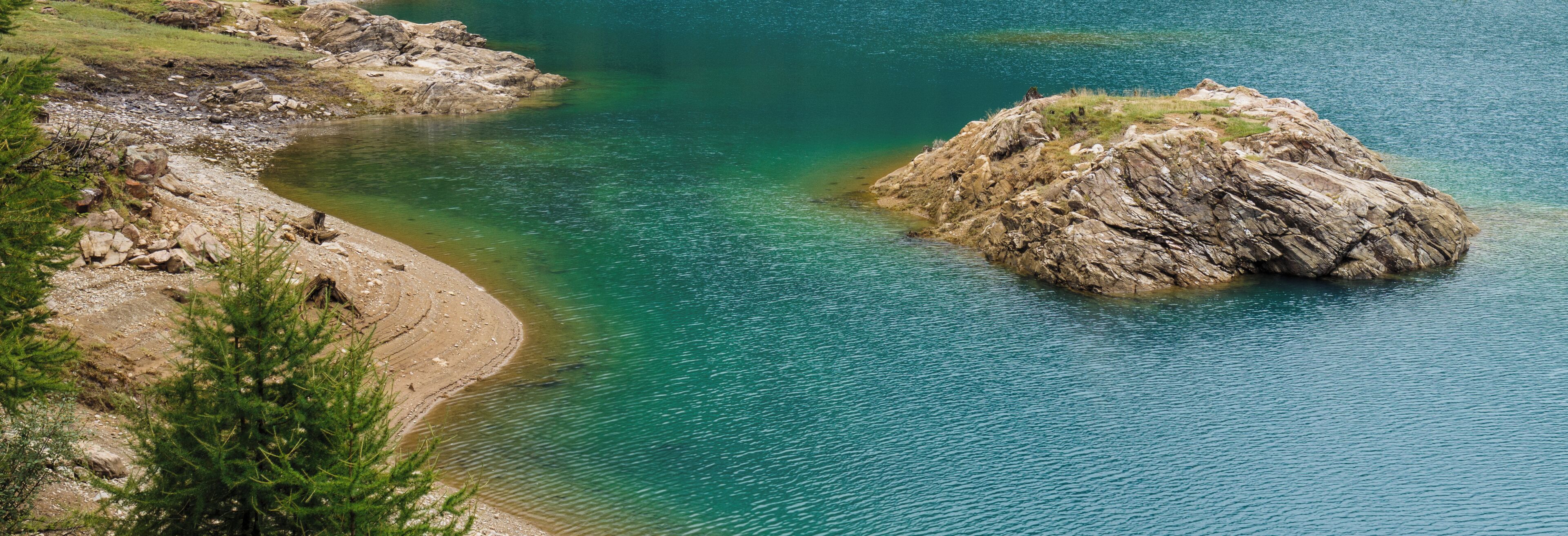 A clear turquoise lake with rocky shores and a prominent hill in the center.