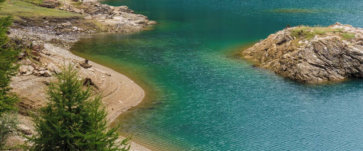 A clear turquoise lake with rocky shores and a prominent hill in the center.