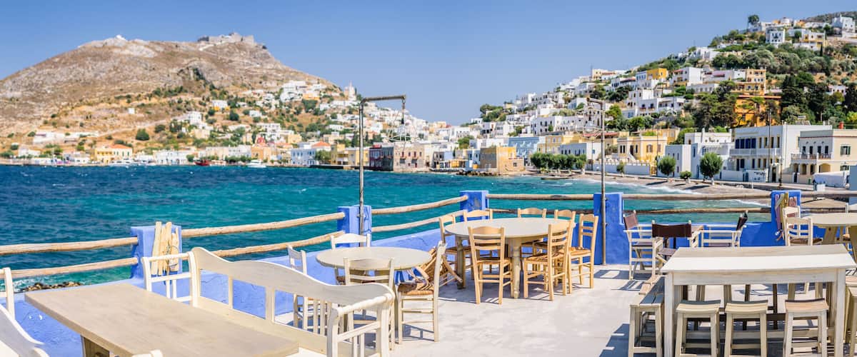 A coastal town with a mountain in the background, blue-painted buildings, and a clear blue sea.
