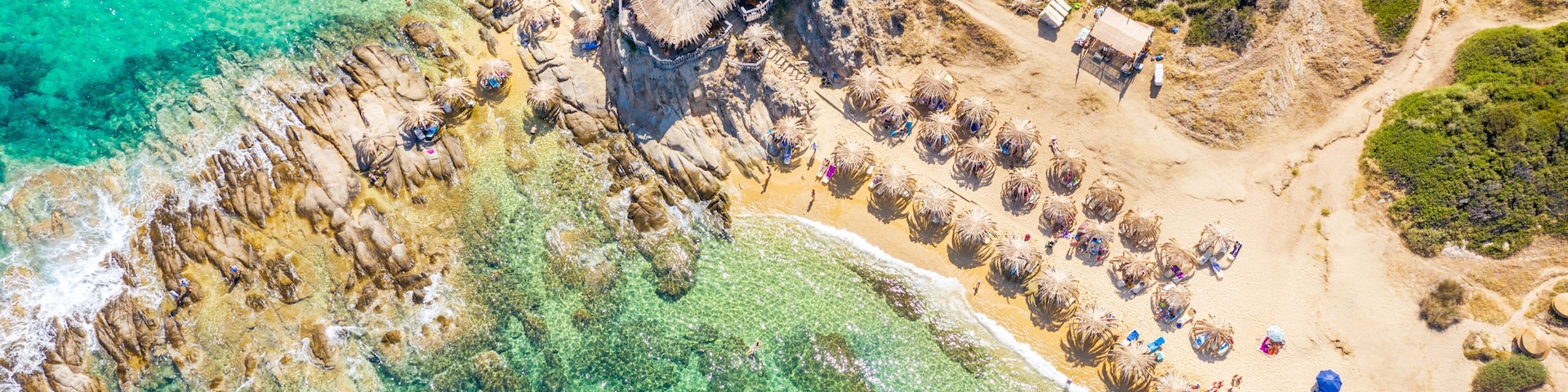 Un paisaje costero con aguas turquesas cristalinas, acantilados rocosos y una playa arenosa con construcciones de techo de paja.