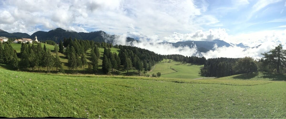 A green field with a church, trees, and mountains in the background.