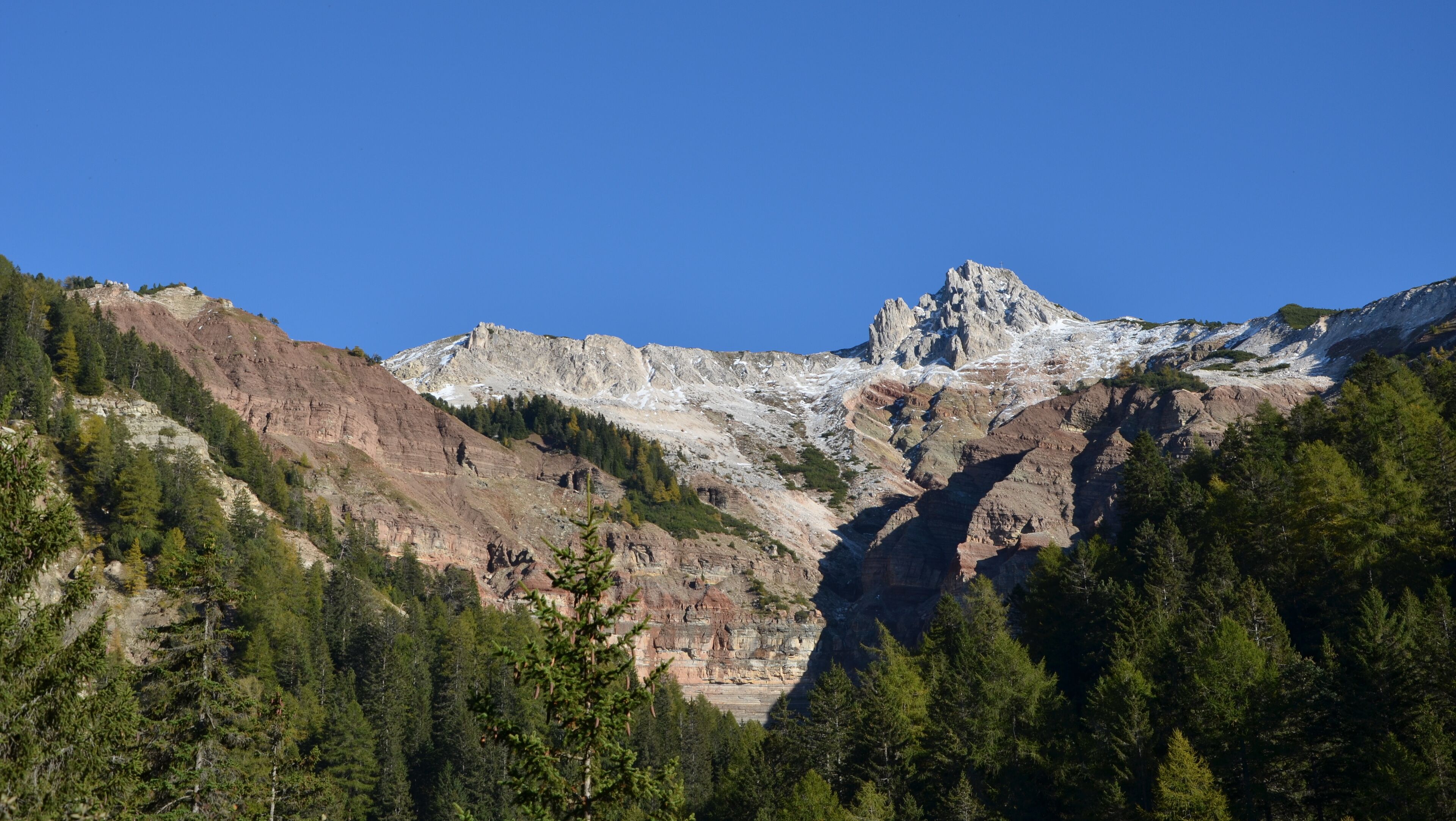 A rugged mountain range with a prominent peak, dense forested slopes, and a clear blue sky.