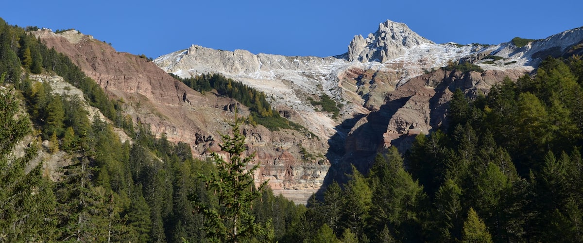 A rugged mountain range with a prominent peak, dense forested slopes, and a clear blue sky.