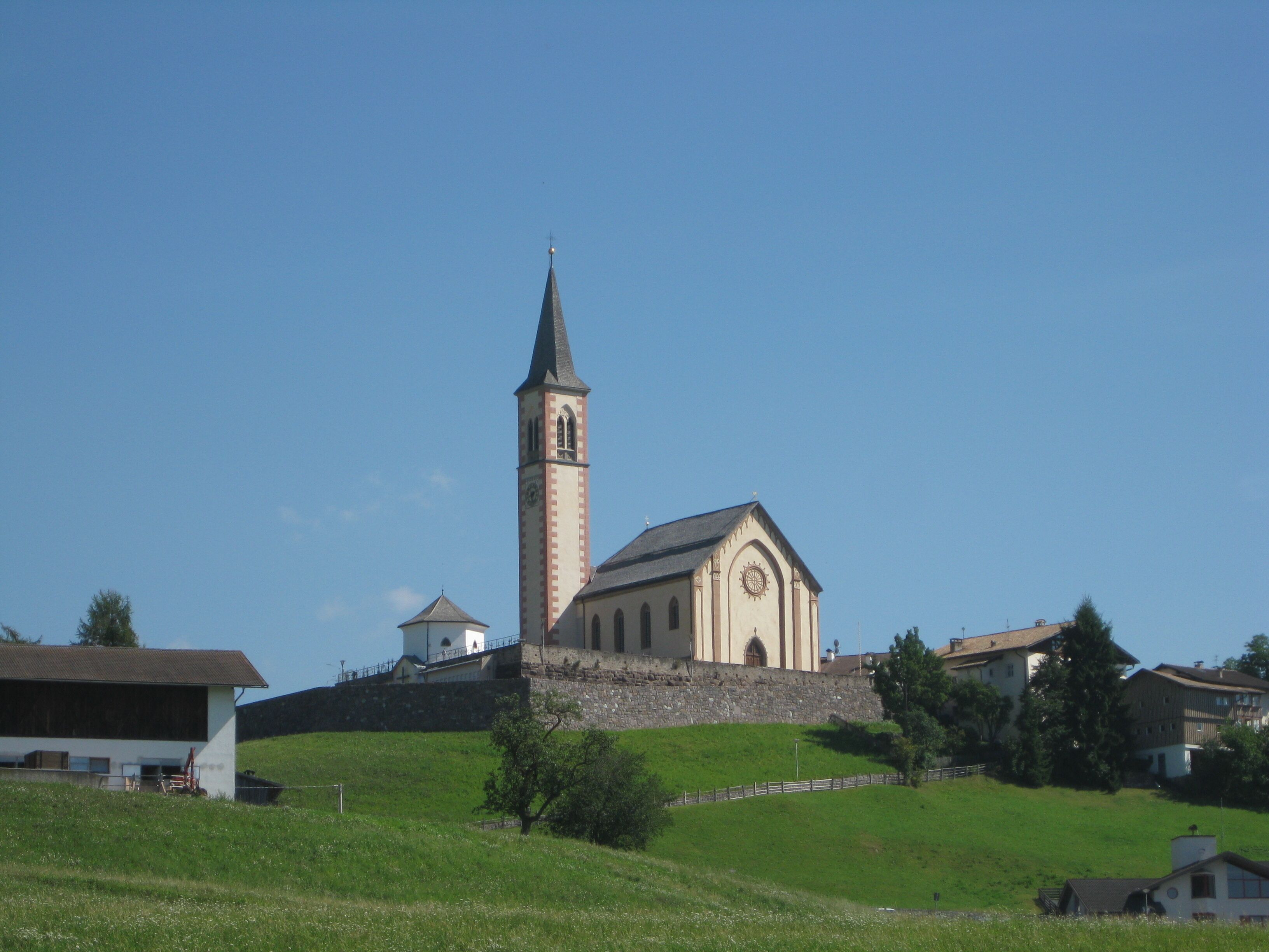 Une église dotée d’un haut clocher et d’un bâtiment plus petit, situés sur une colline verdoyante.