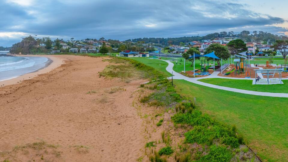 A beach with a park and houses in the background.