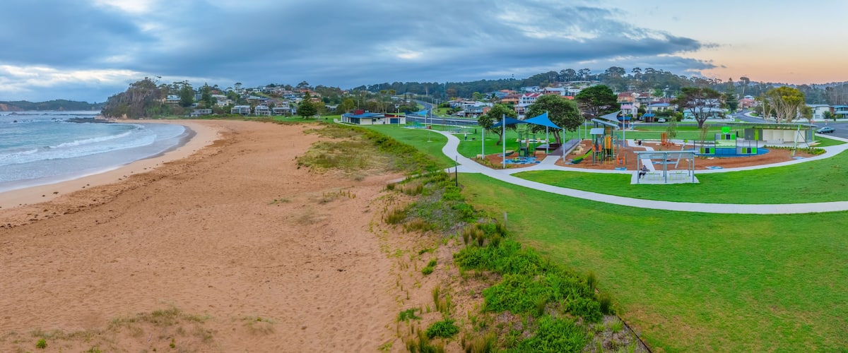 A beach with a park and houses in the background.