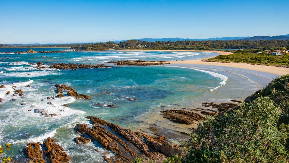 A coastal landscape with rocky outcrops, clear turquoise waters, and a sandy beach.