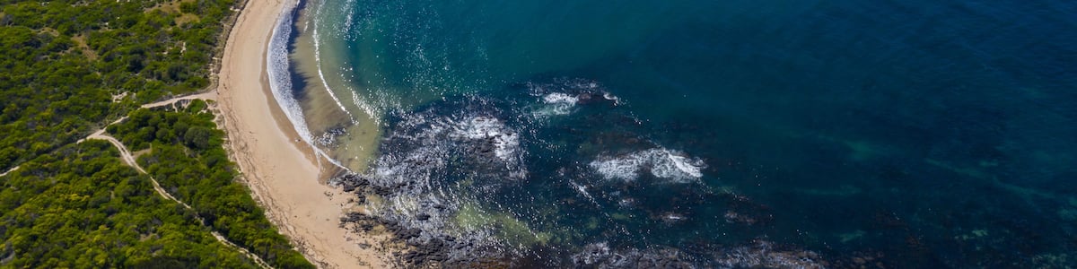 An aerial view of a coastal landscape with a sandy beach, a small island, and clear blue waters.