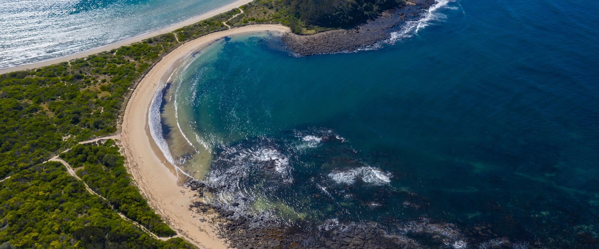An aerial view of a coastal landscape with a sandy beach, a small island, and clear blue waters.