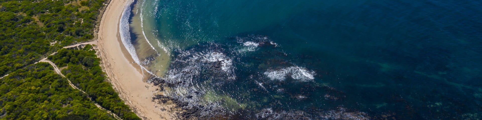 An aerial view of a coastal landscape with a sandy beach, a small island, and clear blue waters.