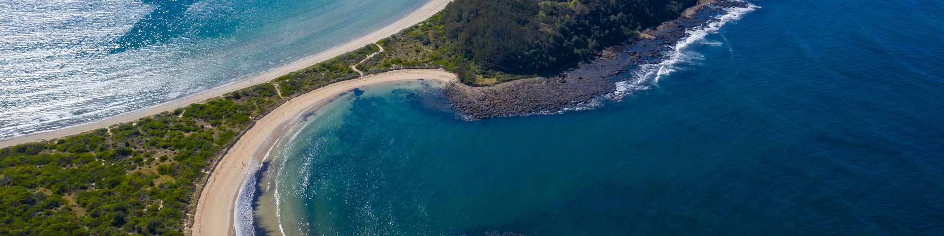 Vista aérea de un paisaje costero con una playa arenosa, una pequeña isla y aguas azul cristalino.