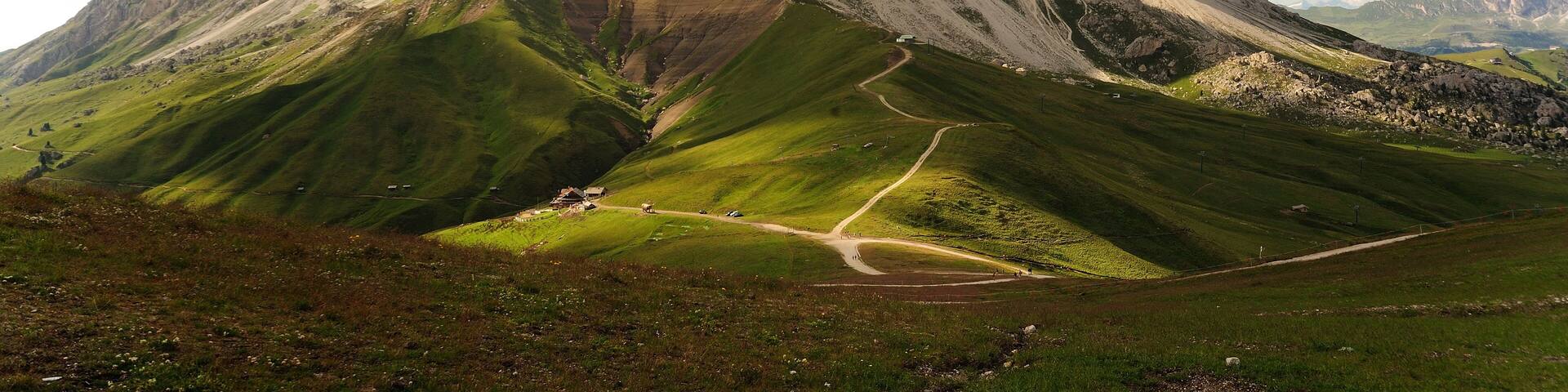 A mountain landscape with a prominent rocky peak and a winding road leading to a small building.