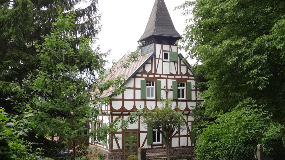 Ein traditionelles Fachwerkhäuschen mit einem steilen Walmdach und einem kleinen Turm.