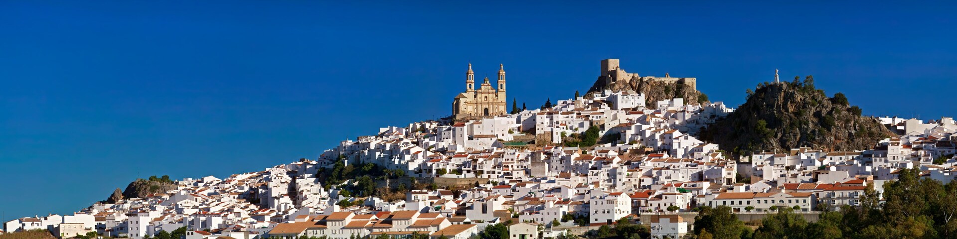 A coastal town with white buildings, a prominent church with a bell tower, and a castle on a hill.
