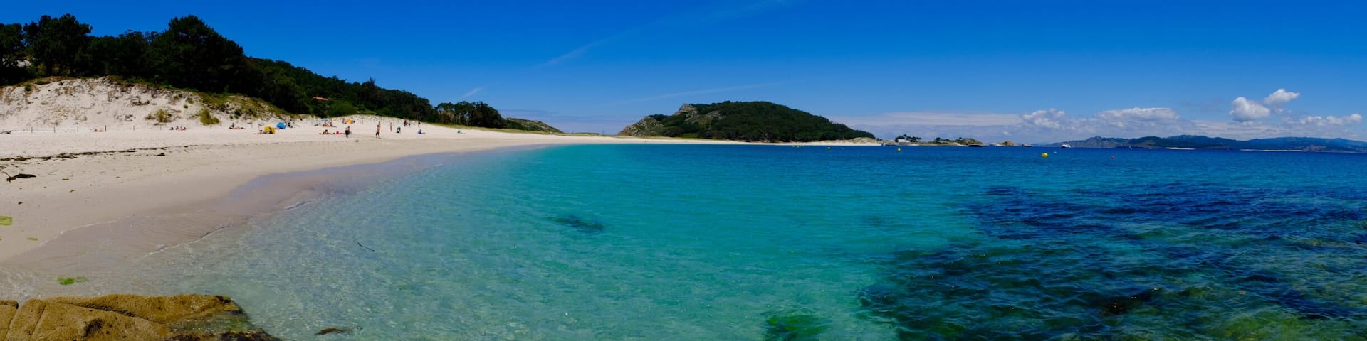 A beach with clear turquoise waters, sandy shores, and rocky outcrops.