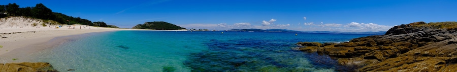 A beach with clear turquoise waters, sandy shores, and rocky outcrops.