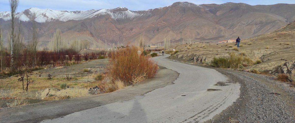 A winding road in a mountainous area with sparse vegetation and distant snow-capped peaks.