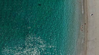An aerial view of a beach with clear turquoise water, several beach umbrellas, and people sunbathing.